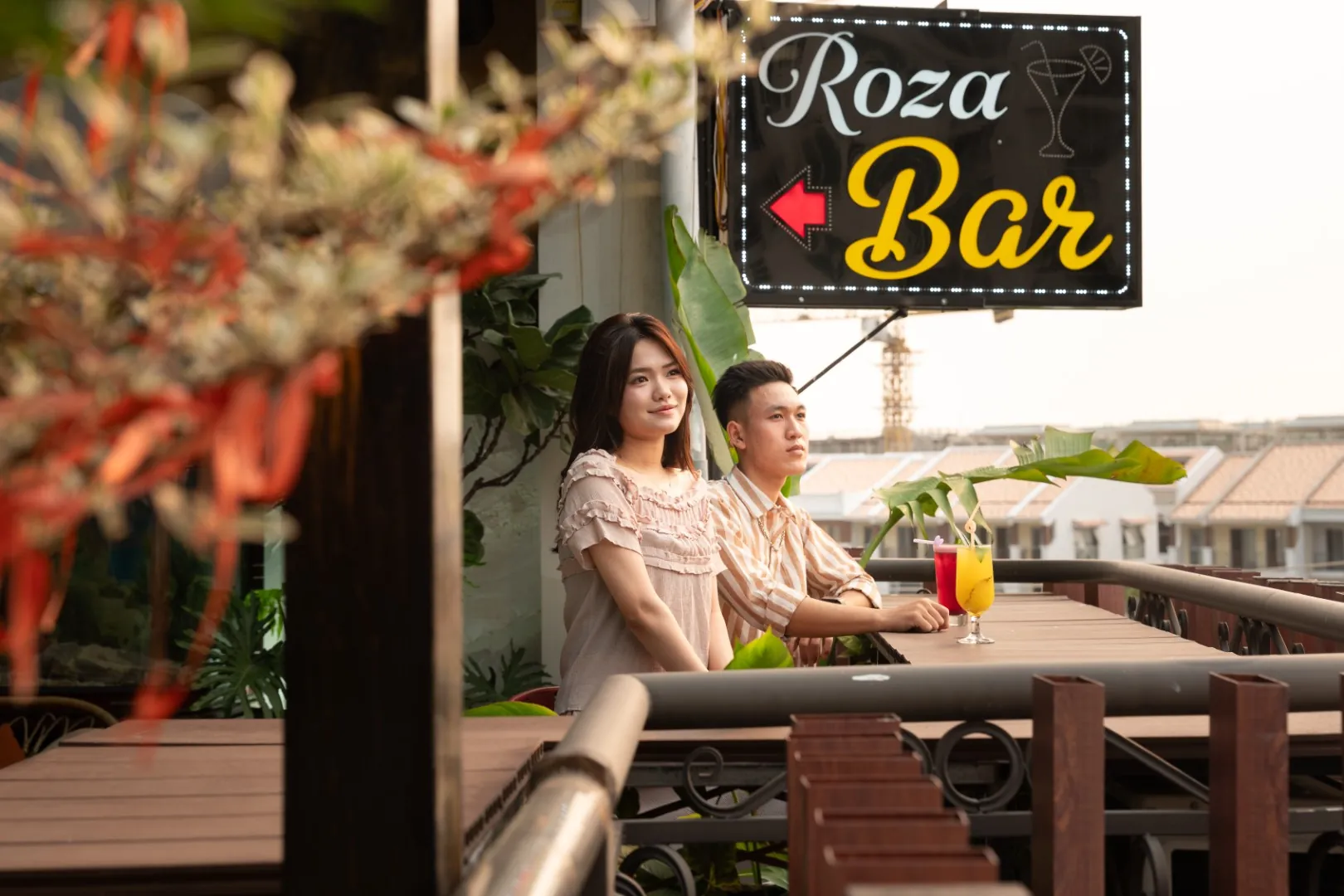 Couple with drinks under the Roza Bar sign on the rooftop in Cat Ba